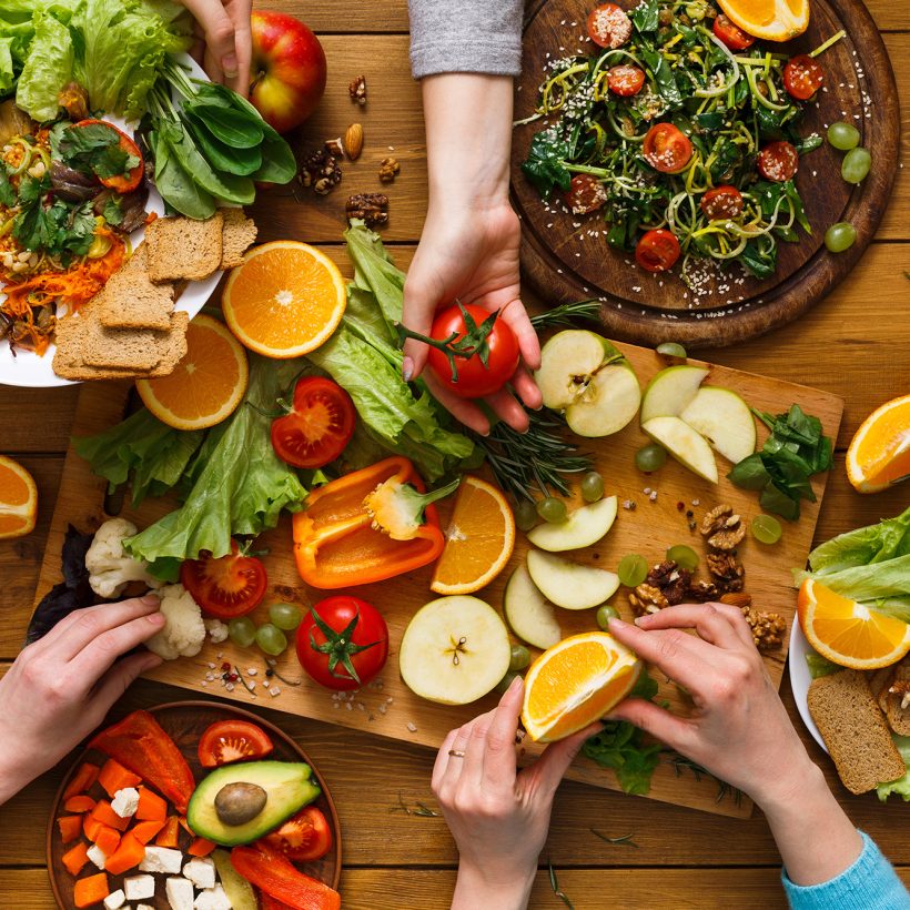 Healthy vegetarian dinner table. Women at home together, eating fruits and vegetables, top view, flat lay, crop