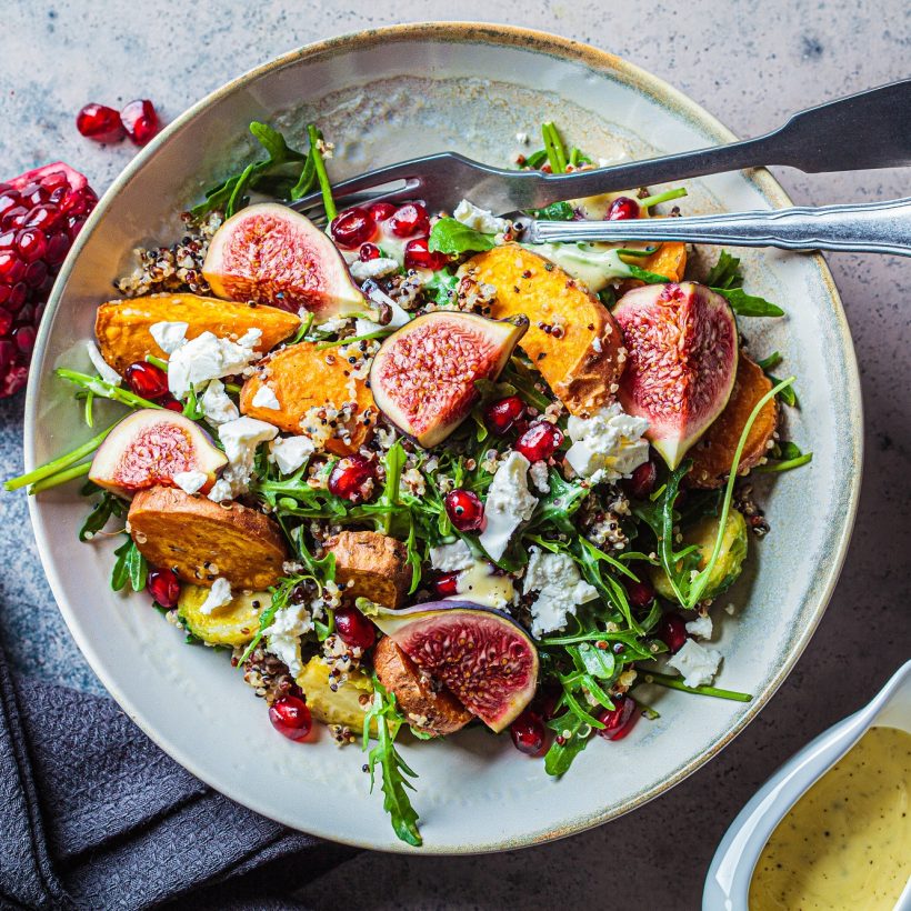 Warm autumn quinoa salad with baked vegetables (sweet potato, Brussels sprouts), figs, feta cheese and pomegranate, top view.